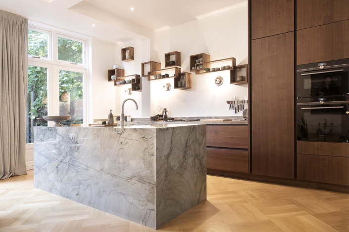 Strakke keuken met kasten met warme donkere houten fronten en grijs stenen keukeneiland
