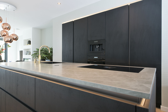 Moderne keuken met zwarte hoge kastenwand en kookeiland met grijs stenen blad