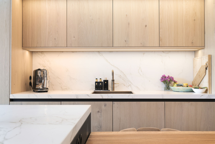 Houten keukendeuren in strakke keuken met wit marmeren aanrechtlbad en -achterwand