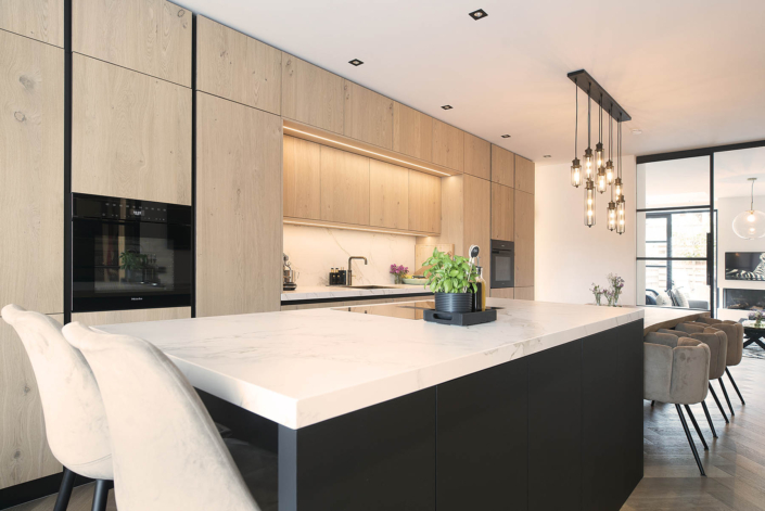 Strakke keuken met houten fronten en keukeneiland met wit stenen blad en zwarte fronten