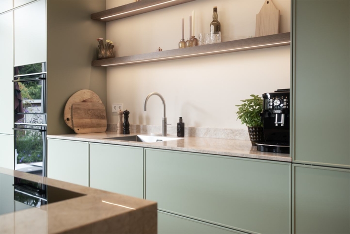 Spoelgedeelte in lichtgroene maatwerkkeuken met houten wandplanken Lichtgroene keuken op maat met open planken en hoge kastenwand