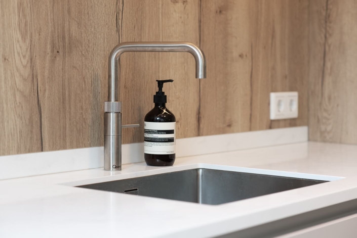 Detail van Quooker kraan en spoelbak in lichte maatwerkkeuken met houten nis
